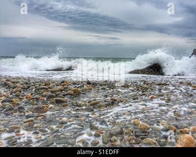 Waves breaking over rocks on pebbly beach Stock Photo