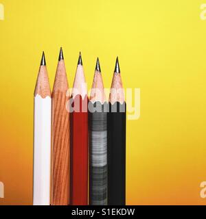 A close-up shot of five different and newly sharpened pencils against a bright yellow background.