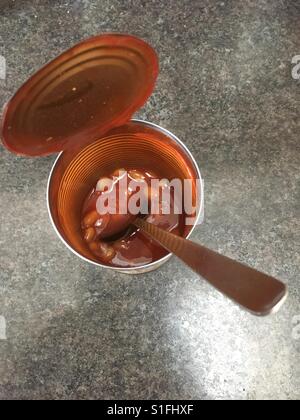An open half eaten tin of beans with a spoon left in the tin Stock Photo