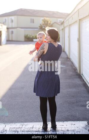 Hip young mom with tattoos and short hair holding baby daughter Stock Photo