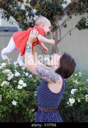 Hip young mom with short hair and tattoos holding baby girl daughter in air smiling Stock Photo