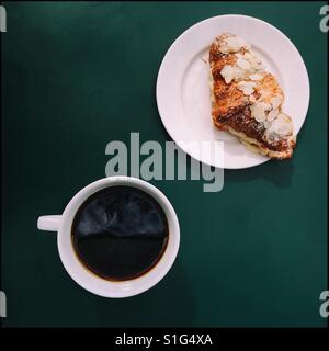 A cup of coffee and an almond croissant on a green table Stock Photo