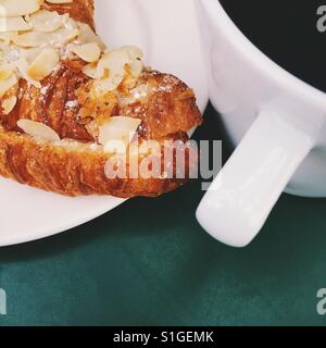 A fresh cup of black coffee and an almond croissant on a green table Stock Photo