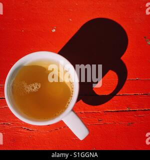 An overhead close-up shot of a fresh cup of herbal tea on a red wooden table. A simple composition with a dark shadow Stock Photo