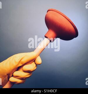 A man's hand in a yellow rubber glove holding a plunger Stock Photo