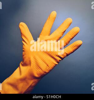 A man's hand in a yellow rubber glove against a blue background Stock Photo