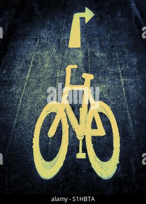 The yellow symbol sign of a bicycle - used to indicate a cycle lane. The arrow pointing right tells cyclists they need to turn right up ahead. Photo Credit - © COLIN HOSKINS. Stock Photo