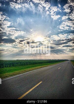 Awesome photo of sun rays bursting through clouds on a Kansas deserted road next to a corn field. Stock Photo