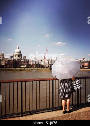 Woman in smart dress holding an umbrella as she stands against London view with st Paul's cathedral visible on the horizon Stock Photo