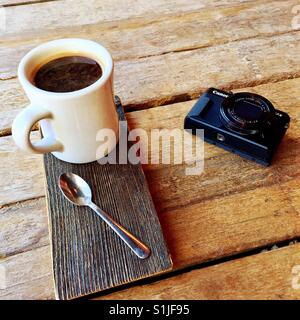 A fresh Americano beverage and a compact Canon camera on a wooden table Stock Photo