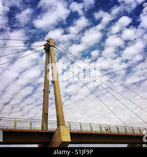 A man walks across a pedestrian bridge under an interesting cloudy sky Stock Photo