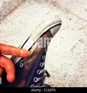 A man sitting cross legged and poking his finger in a hole in his well worn Converse shoe Stock Photo