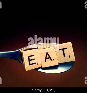 Close up of a spoon with wooden letters on it spelling the word eat Stock Photo