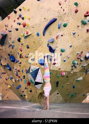 A girl performs a handstand in front of an indoor climbing wall. Stock Photo