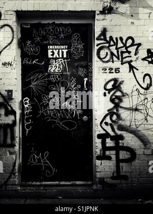 An emergency exit door and the surrounding wall covered in tagging and graffiti Stock Photo