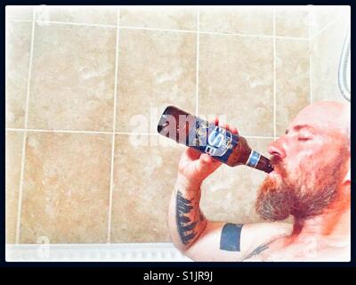 Sweating man in hot bath drinking Fullers ESB straight from the bottle. Stock Photo