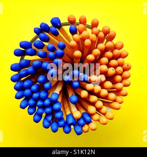 An overhead shot of a bunch of blue and orange tipped matchsticks in a glass container Stock Photo