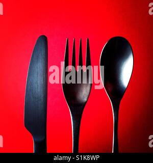 A close up overhead shot of a knife and a fork and a spoon above a red background Stock Photo