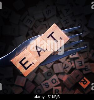 Close up of a fork with wooden letters on it spelling eat above a background with more wooden letters Stock Photo