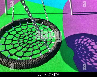 A new swing casts an interesting shadow onto the colourful ground in a children's playground. A graphic image with interesting colours & shapes. Photo Credit - © COLIN HOSKINS. Stock Photo