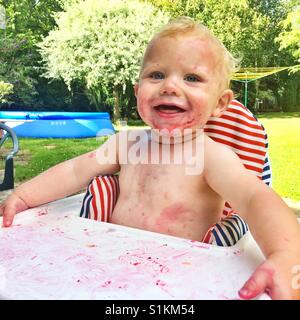 Ten month old baby boy sitting in a high chair in the garden. Stock Photo