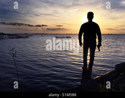 A man with a gun at sunset in front of a lake