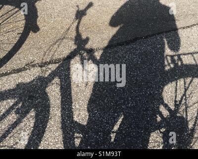 Close up shadow on asphalt of person standing by bicycle. Not fully figured. Stock Photo