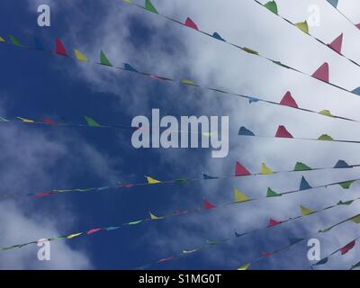 Many strands of multi-coloured bunting fluttering against a blue summer sky with scattered clouds. Stock Photo