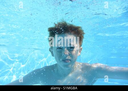 Teenage boy underwater in a swimming pool, looking into camera Stock Photo