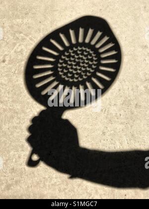 Crescent-shapes of a partial solar eclipse within a sun shape, in the shadow of a colander. Stock Photo