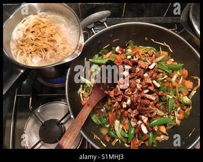 Stir fried chicken and vegetables with egg noodles being prepared in the hob. Stock Photo