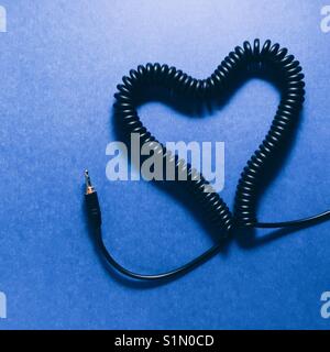 A coiled headphone cable made into a heart shape on a blue background Stock Photo