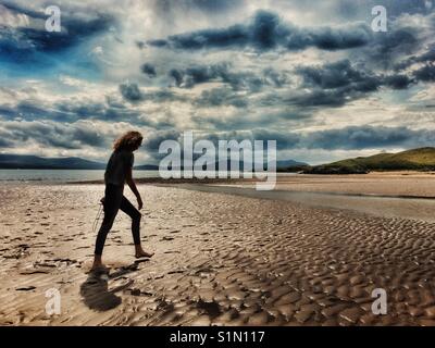 Lone figure of young girl walking barefoot on an a deserted beach at low tide (Newborough beach, Anglesey)
