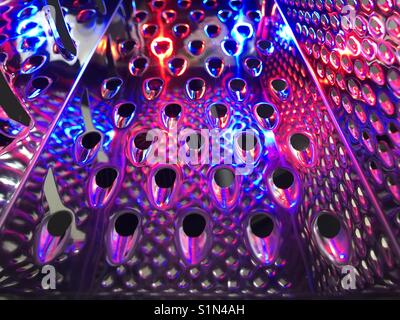 Colourful abstract of inside of cheese grater with coloured lights shining through Stock Photo