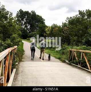 Young couple and a dog on a path through shrubs and trees on a warm day. Concepts family, outing, outdoors, leisure, de stressing, communing with nature, fresh air Stock Photo