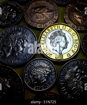 New Pound Coin glows amidst older coins, in colour. Stock Photo