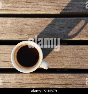 A simple overhead composition of a fresh Americano espresso drink on a wooden bench with a long shadow Stock Photo