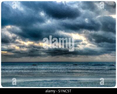 Sunrise storm clouds stir over a calm ocean shoreline Stock Photo