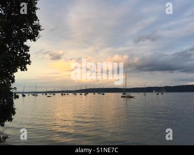 Lake with sailing boats in the evening by sunset, Starnberger See and Roseninsel, wild life park with trees and water in dramatic orange light Stock Photo