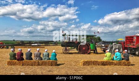 Young woman in traditional Amish dress selling on bales of straw watching a farming demonstration. Near Arthur, Illinois, USA. Stock Photo