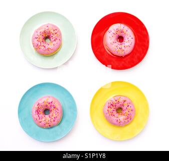 Looking down from above onto for colourful plates with donuts sitting on them that have pink icing with hundreds and thousands Stock Photo