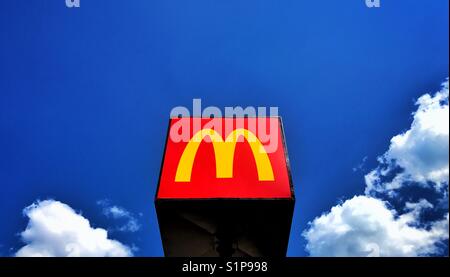 The famous McDonalds yellow M sign can be found outside a fast food restaurant on a Summers day. The sky is blue, the clouds are starting to form. Lots of room for copy. Photo Credit - © COLIN HOSKINS Stock Photo