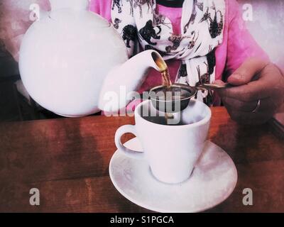 Woman in a restaurant, pouring a cup of tea from a teapot Stock Photo