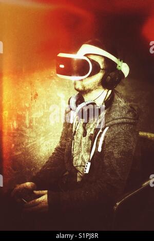 A young man wearing a virtual reality headset and eyepiece and earphones playing on a console video game and getting lost in the moment Stock Photo