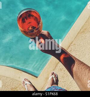 Looking down at man holding glass of Aperol Spritz over swimming pool. Stock Photo