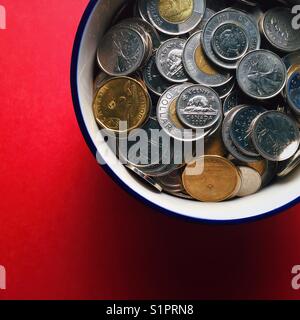 A close-up cropped shot of a bowl full of assorted Canadian coins on a red background Stock Photo