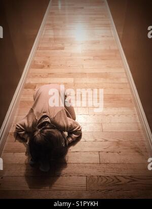 Toddler girl in onesie pjs curled up on hallway floor Stock Photo