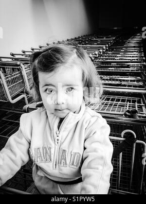 Toddler girl in grocery cart with rows of carts behind her Stock Photo