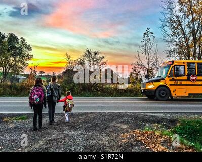 Three girls about to get on school bus in rural Ontario, Canada Stock Photo