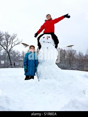Two girls proudly showing off their newly built snowman in Ontario, Canada Stock Photo